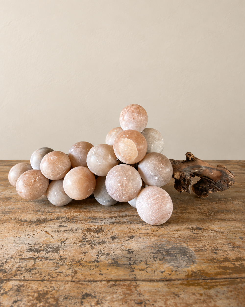 A substantial vintage alabaster grape cluster, attributed to Italy, with softly rounded stone fruit gathered around a richly textured natural wooden stem. Muted shades of peach and smoky grey lend the piece a quiet, painterly quality