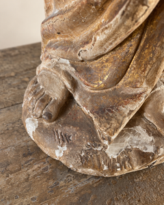 An expressive carved wooden French Antique Madonna, crowned with roses and standing with her gaze gently lowered and one hand resting across her chest. Deeply folded robes and a sweeping mantle give the figure a graceful, sculptural presence, with carved detail continuing around the back.
