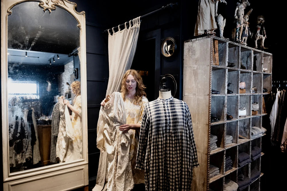 Melissa arranging garments inside Manteau Noir beside an antique mirror and shelving